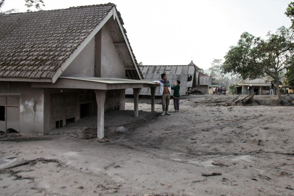 Vesničané stojí poblíž domu v oblasti zasažené erupcí sopky Semeru